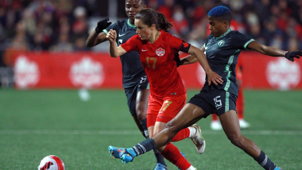 Canadian female soccer player fighting for the ball against two female Nigerian players